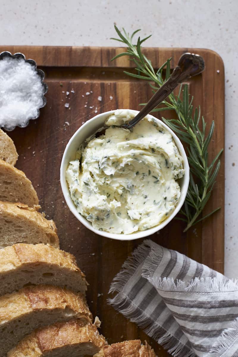 Rosermary Garlic Butter in a bowl on a wooden cutting board.