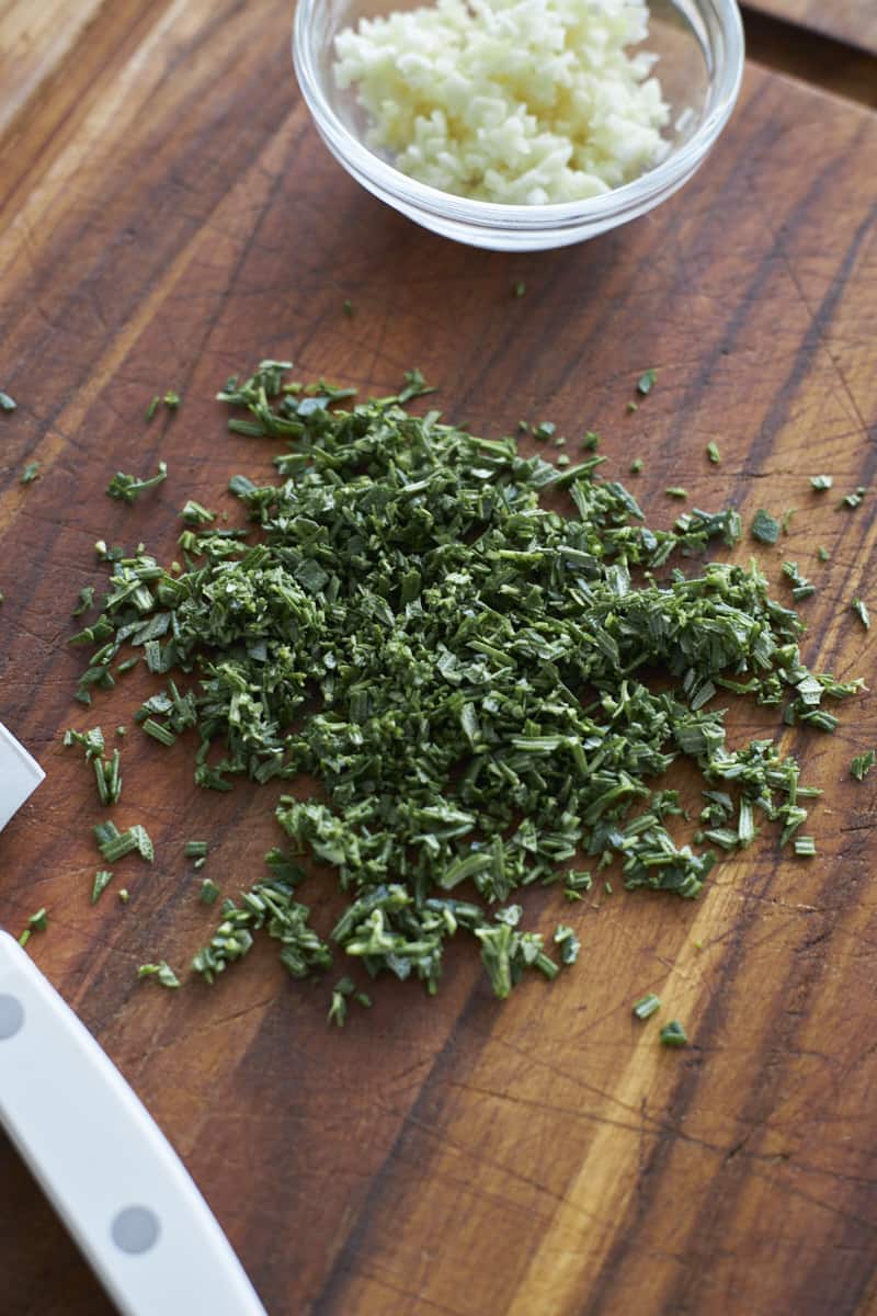 Chopped rosemary on a wooden cutting board.