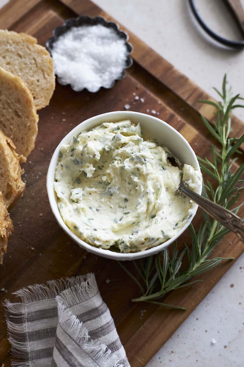 Rosermary Garlic Butter in a bowl on a wooden cutting board. 