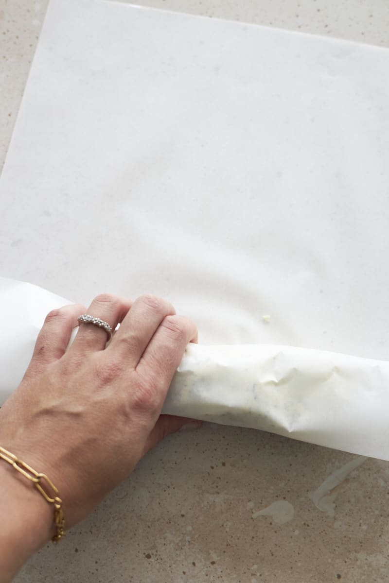 A hand rolling the butter into a parchment paper log.
