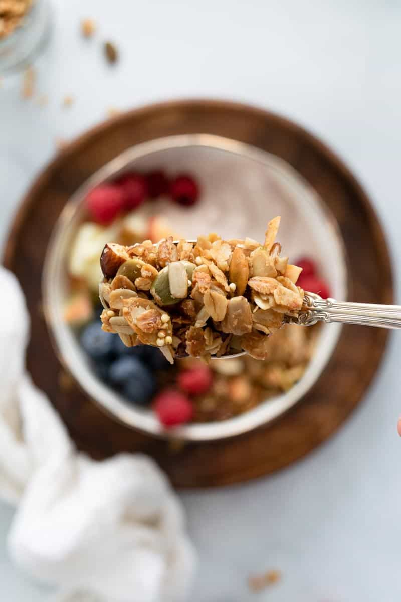 Spoonful of granola over a bowl of yogurt and berries. 