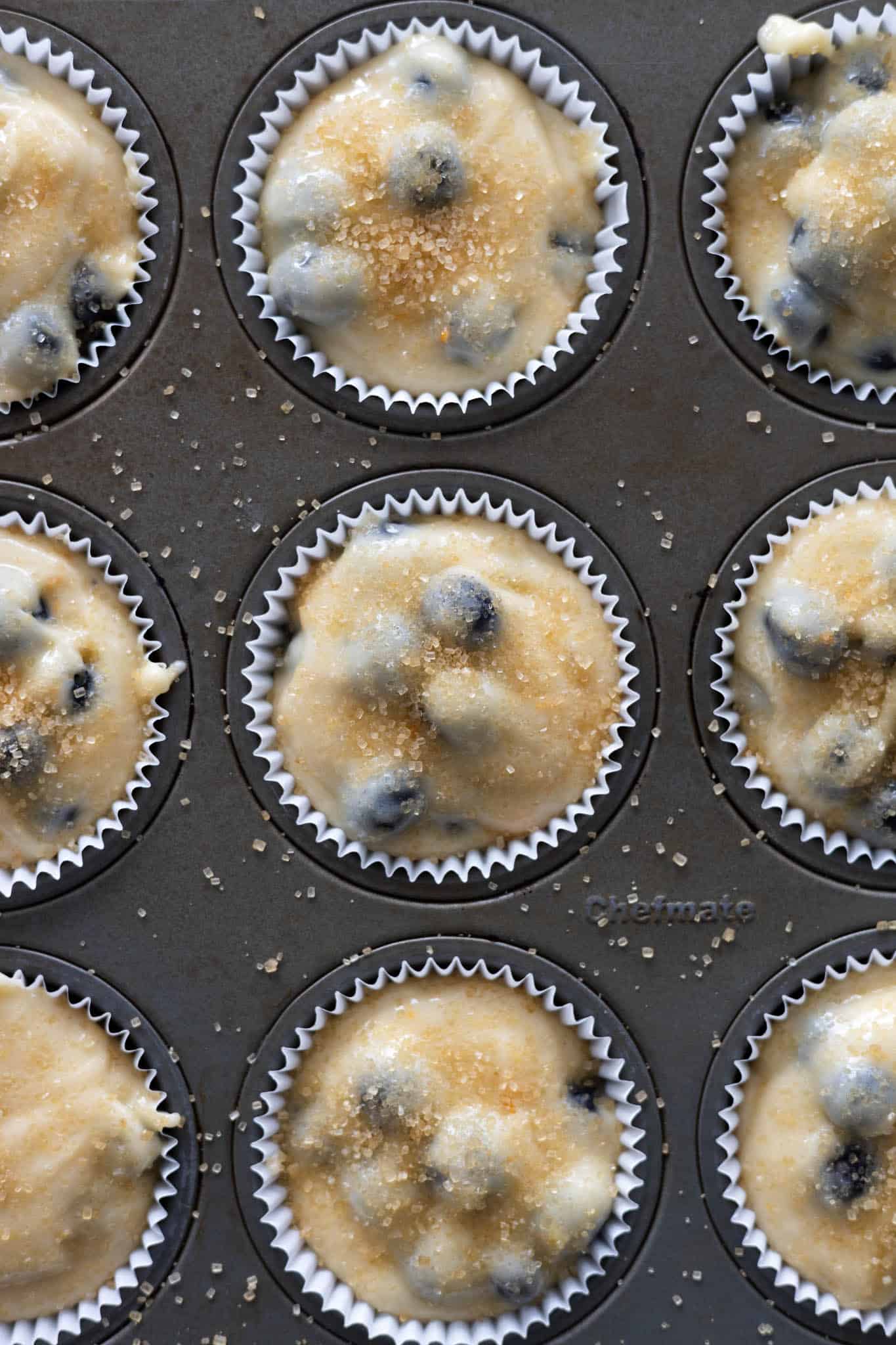 Muffin cups filled with batter and topped with turbinado sugar, ready for baking. 