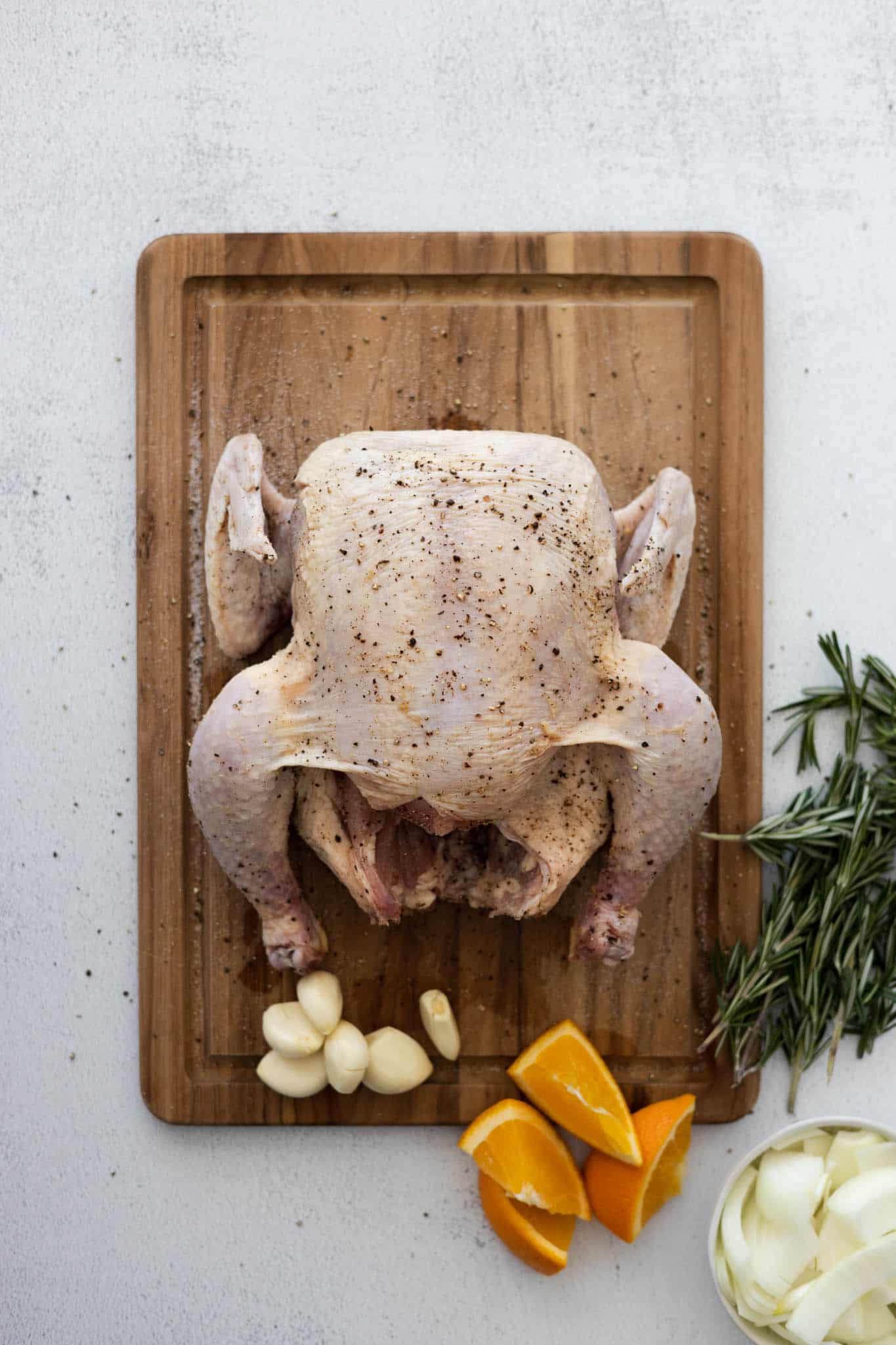 Prepping the raw chicken with salt and pepper, surrounded by the garlic, orange slices, onion and rosemary. 