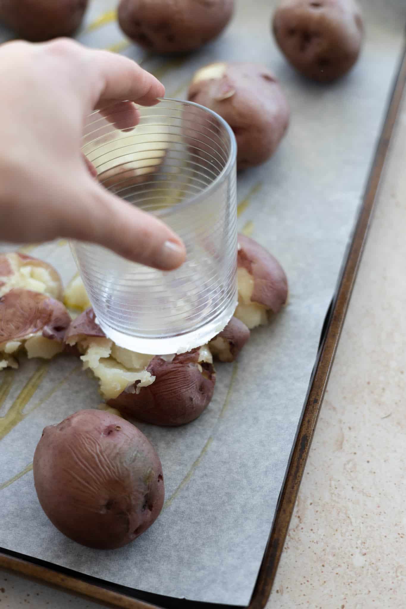 Smashing a potato with the flat base of a glass on a baking sheet. 