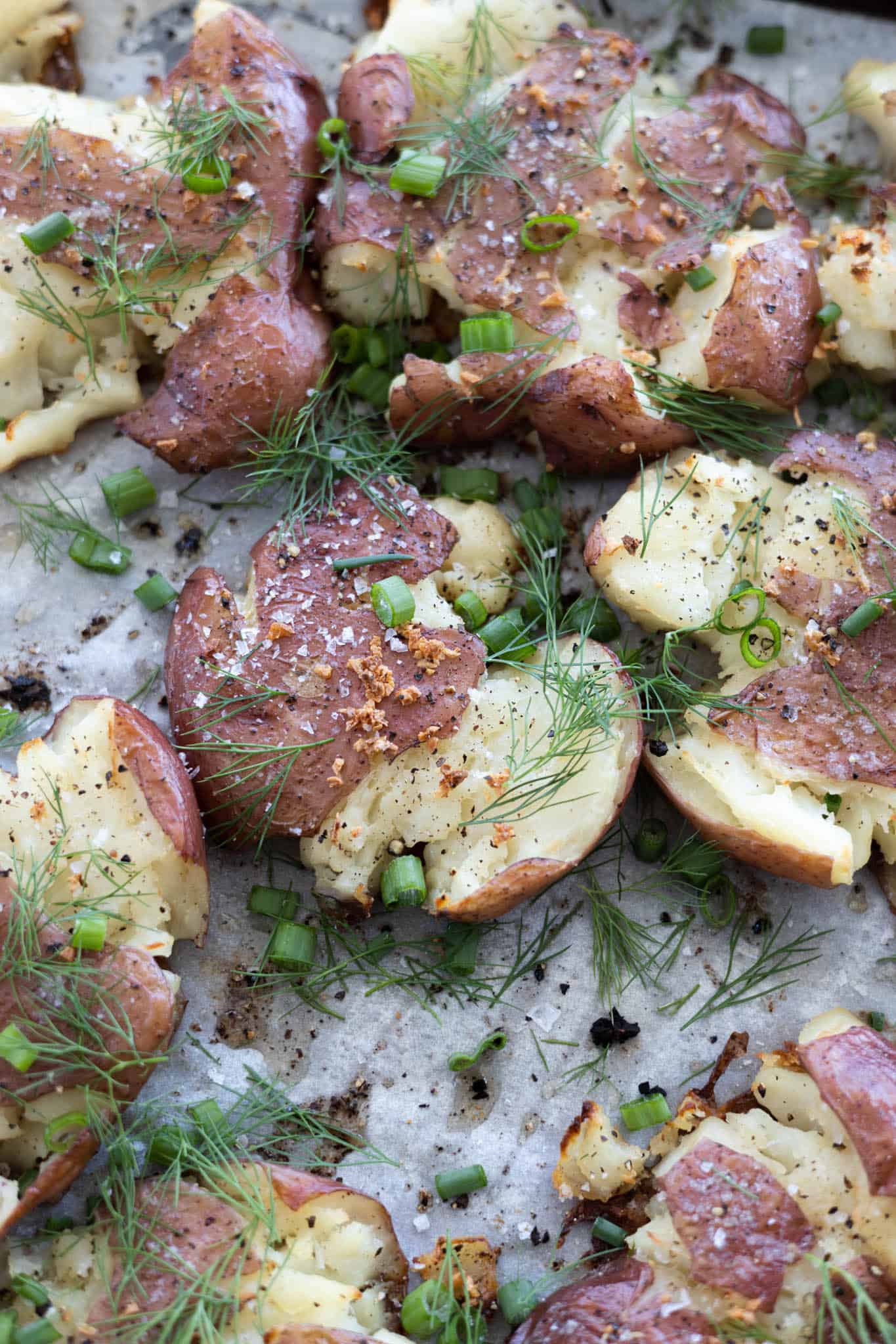 A closeup of smashed potatoes on a baking sheet sprinkled with green onions and dill. 