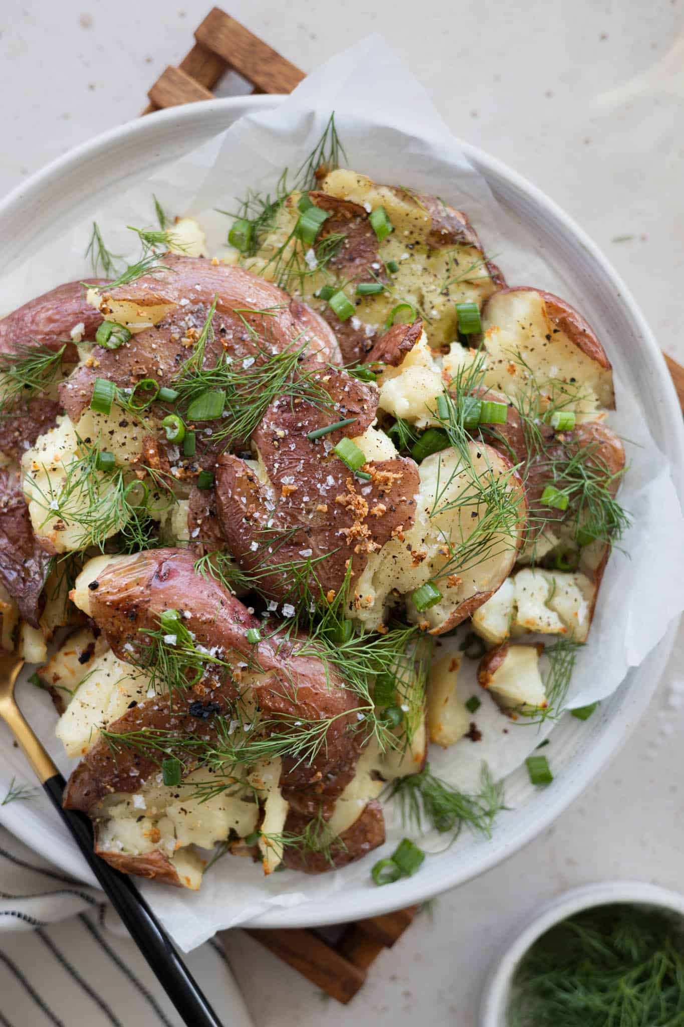 Smashed potatoes with green onions and dill on a serving platter.