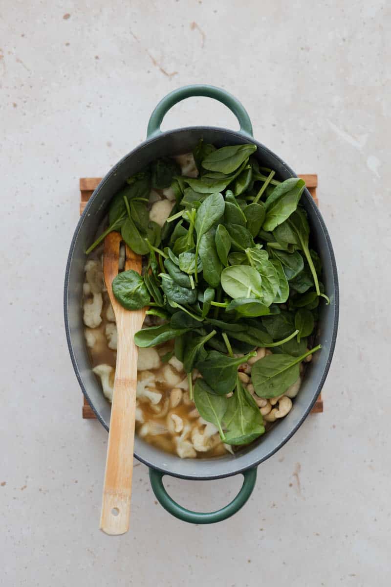 Spinach added to the soup in a Dutch Oven. 