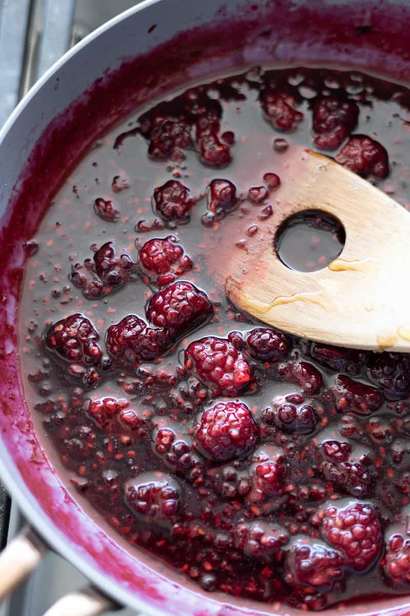 Blackberries simmering and becoming syrupy on the stovetop in a small skillet.