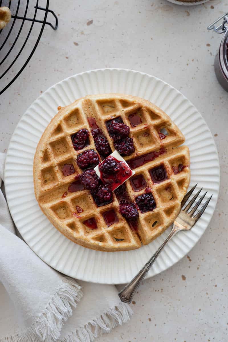 A Cornmeal Waffle with Blackberry Bourbon Maple Syrup on a plate with a fork. 