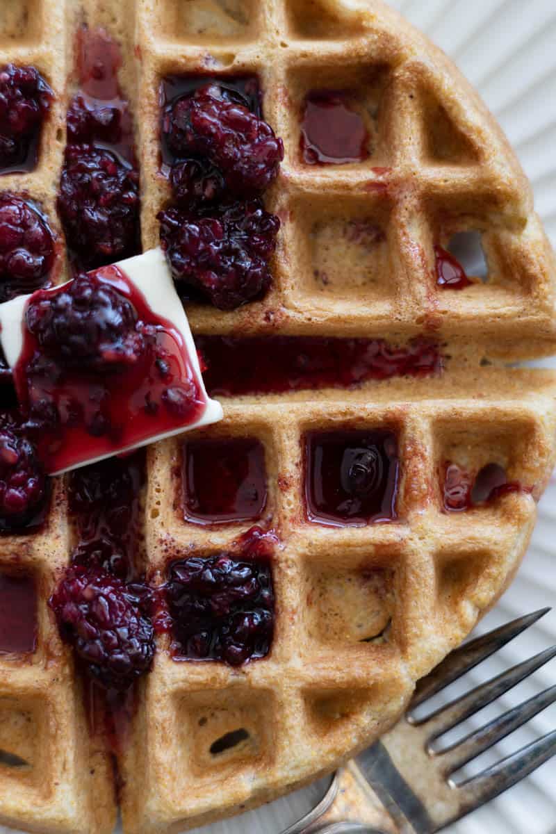 A closeup of Cornmeal Waffles with Blackberry Bourbon Maple Syrup and pad of butter. 