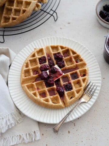 A Cornmeal Waffle with Blackberry Bourbon Maple Syrup on a plate with a fork.