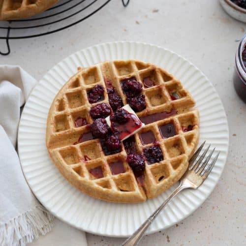 A Cornmeal Waffle with Blackberry Bourbon Maple Syrup on a plate with a fork.