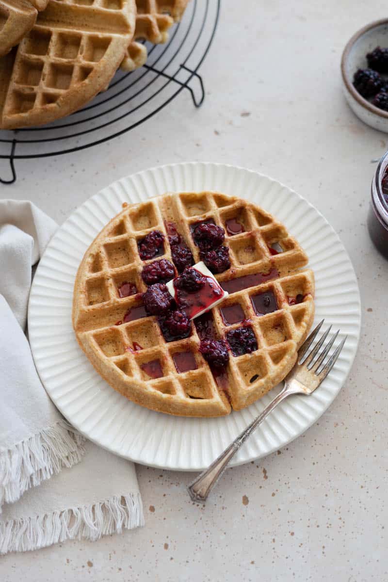 A Cornmeal Waffle with Blackberry Bourbon Maple Syrup on a plate with a fork. 