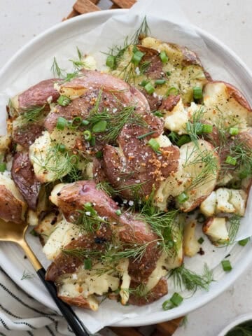 Smashed potatoes with green onions and dill on a white serving platter.
