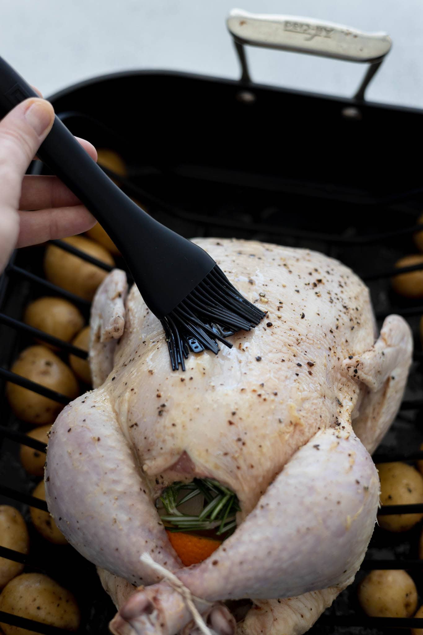 Brushing the bird in a roasting pan with melted butter before putting it in the oven.