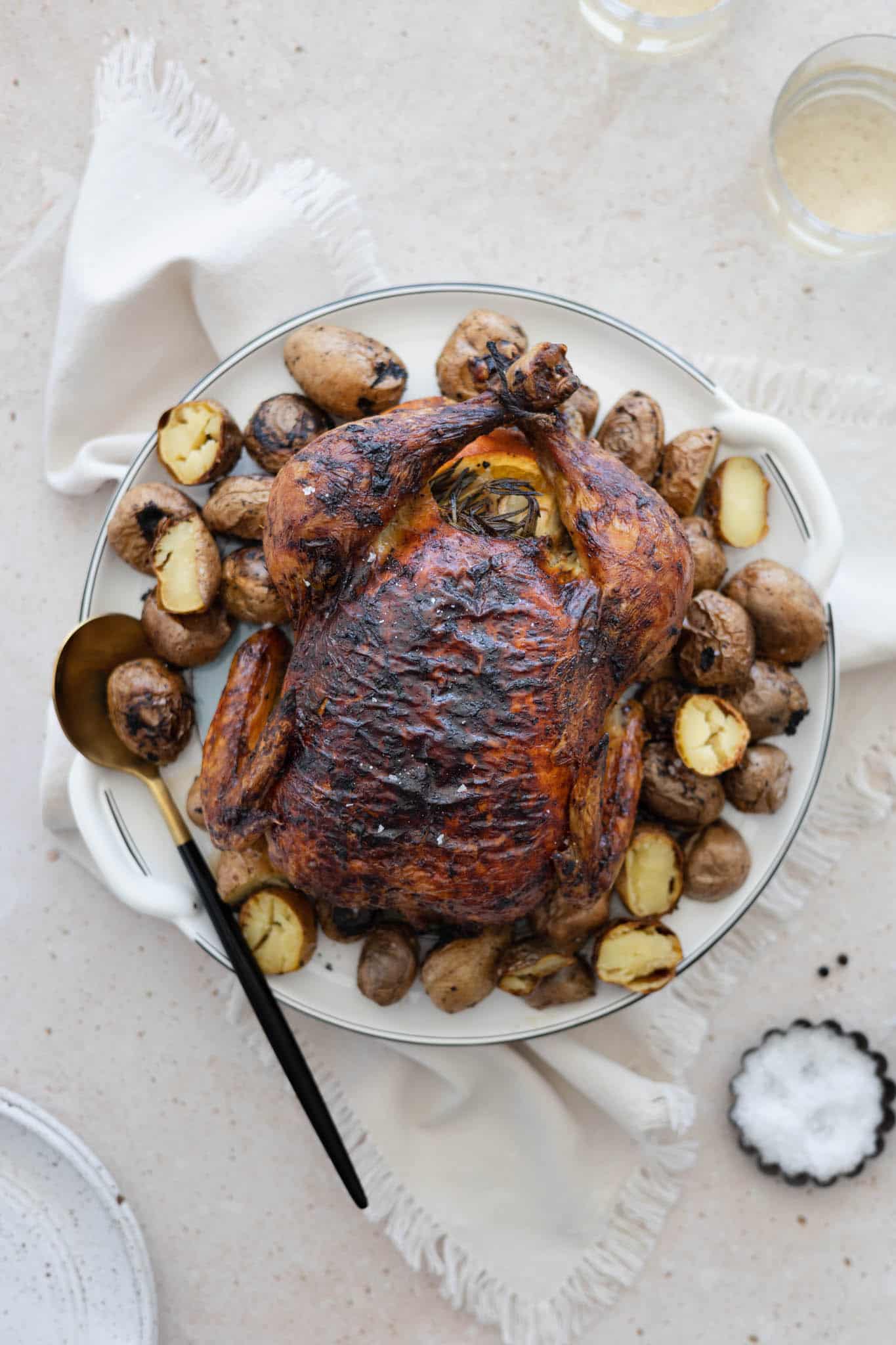 A citrus and herb whole roasted chicken on a platter surrounded by potatoes.