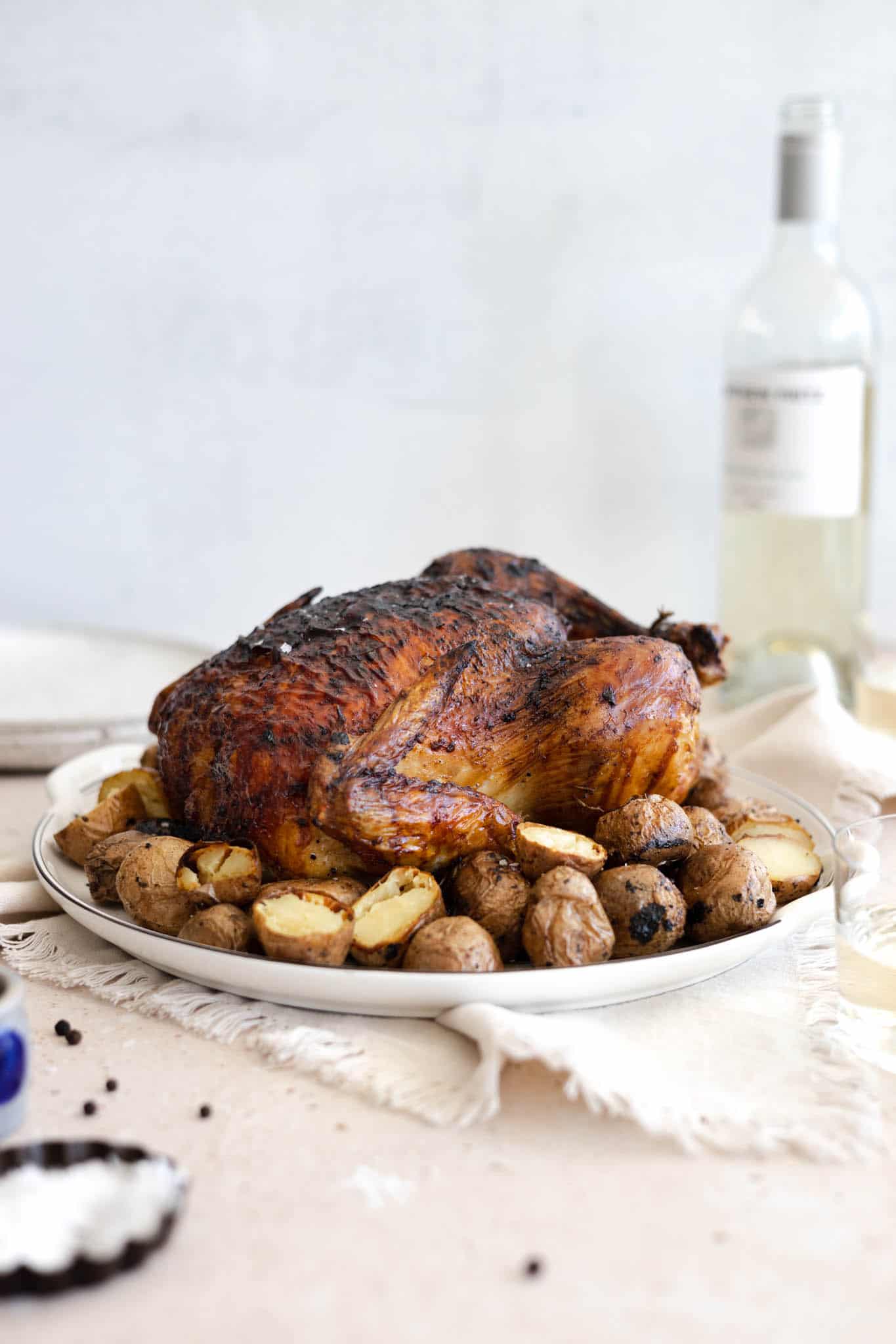 A side view of the chicken on the platter with a bottle of wine in the background.