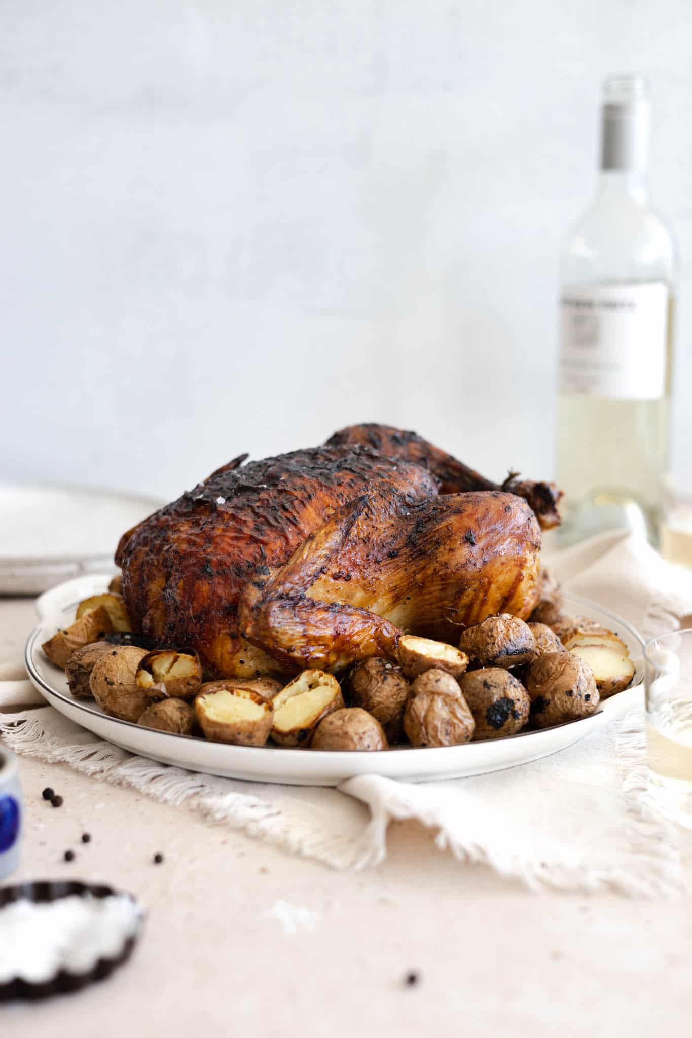 A side view of the chicken on the platter with a bottle of wine in the background. 