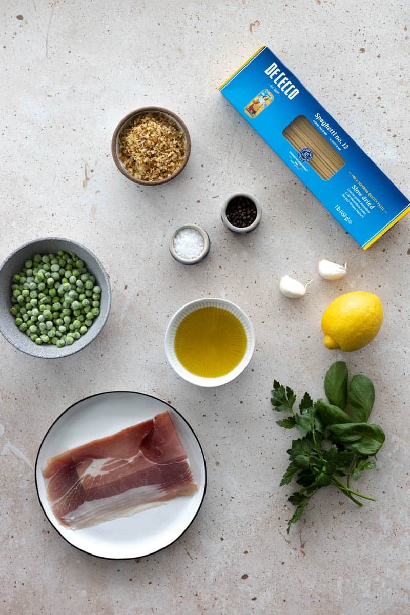 Ingredients for Spring Pasta with Lemon, Peas and Prosciutto in small bowls on a table.