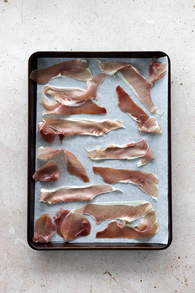 Prosciutto spread out on parchment paper on a baking sheet.