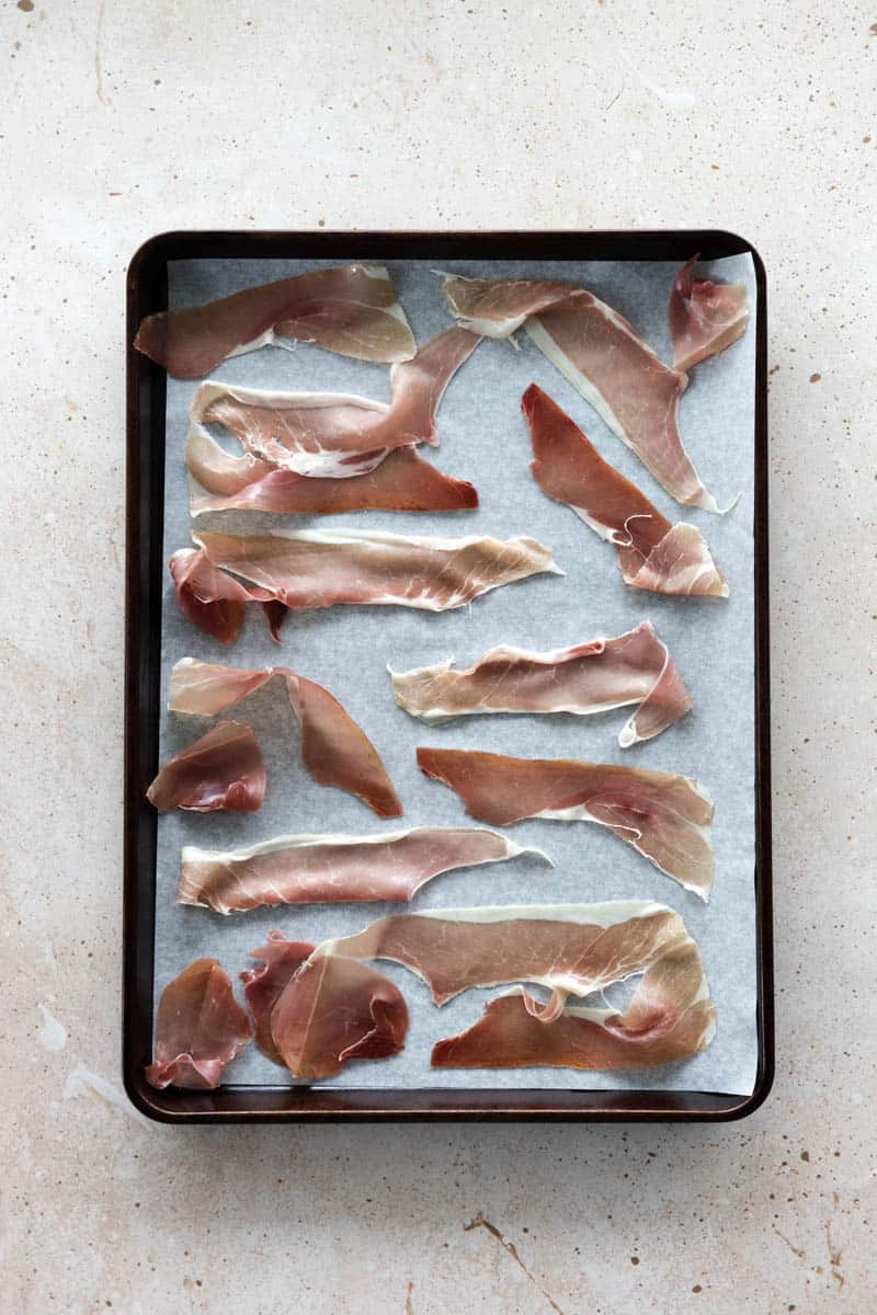 Prosciutto spread out on parchment paper on a baking sheet. 