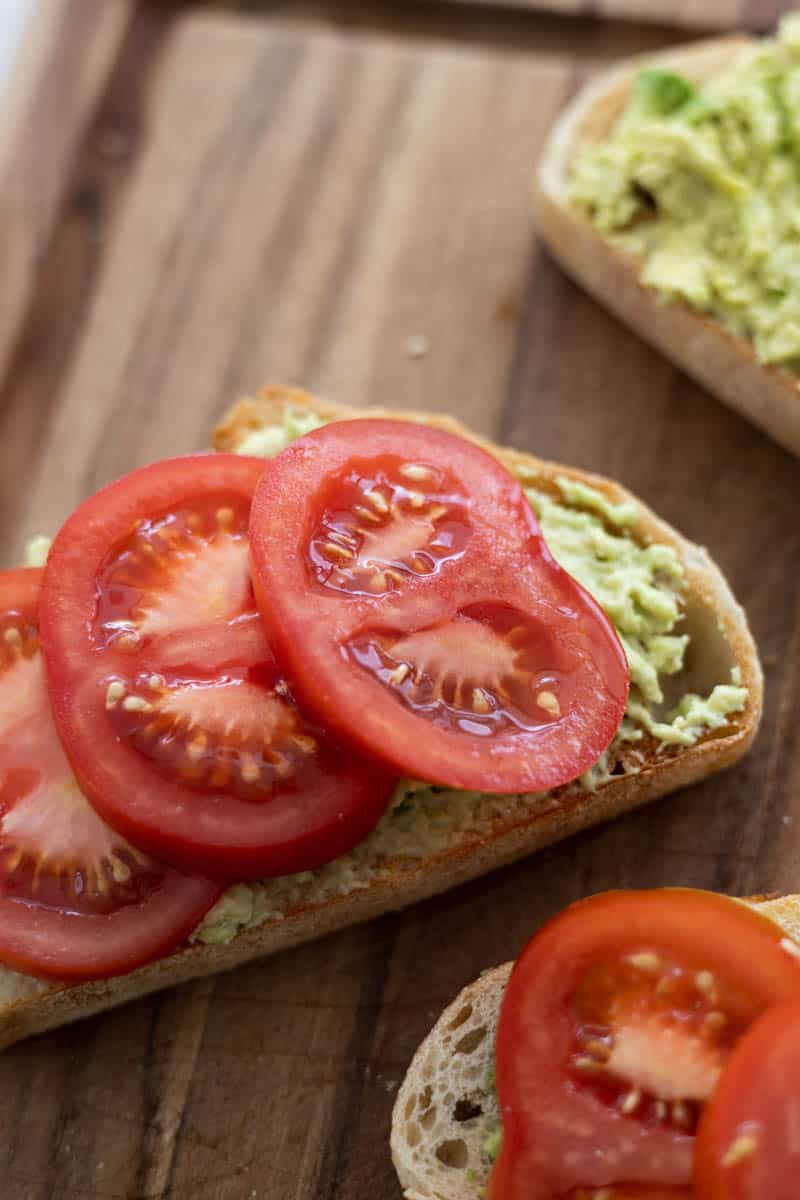 Tomato slices on top of the smashed avocado on the toast.