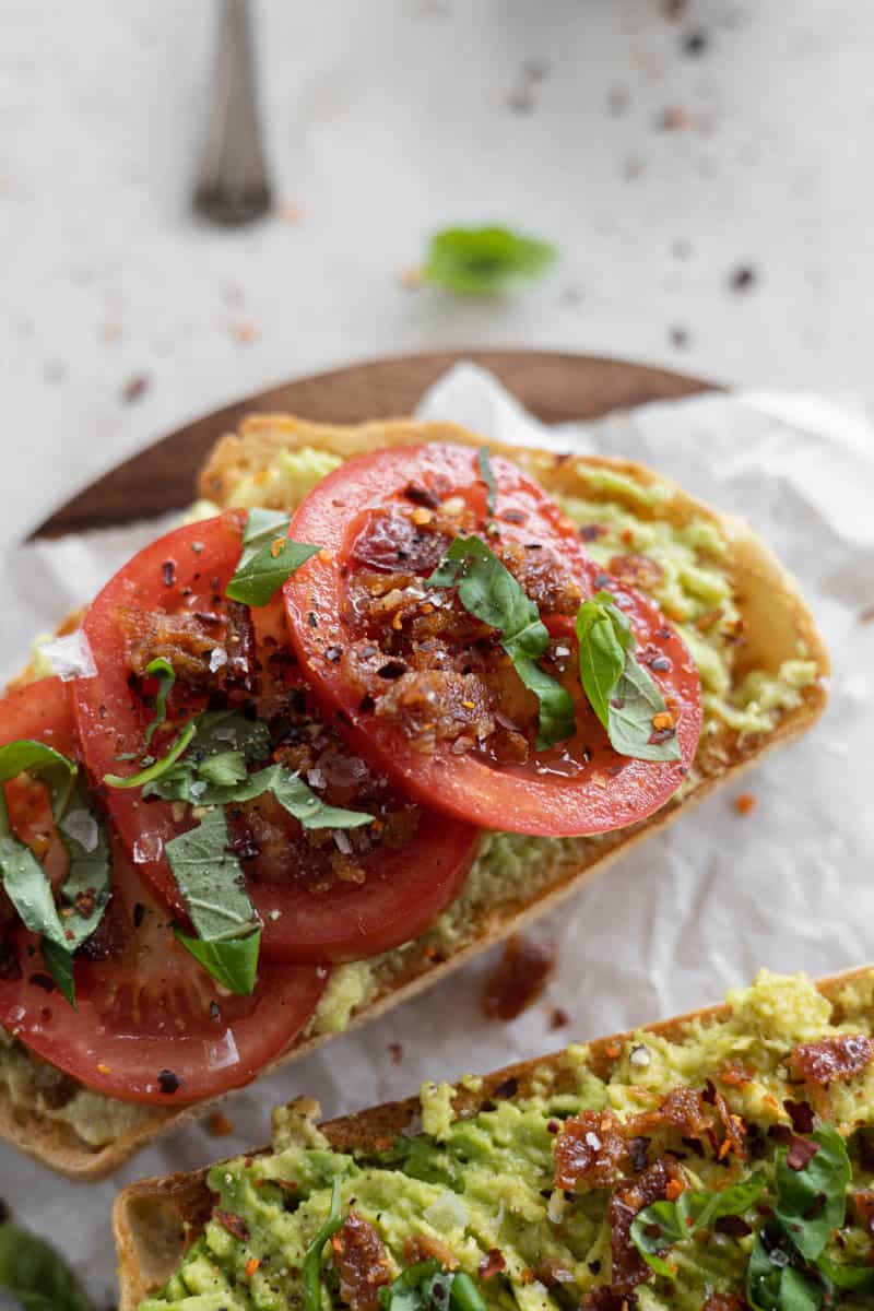 Avocado toast with tomato on a wooden cutting board.
