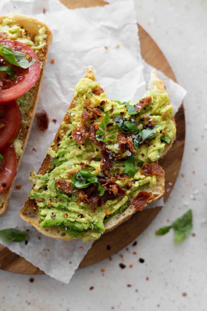 Avocado toast with crumbled bacon and a bite missing.