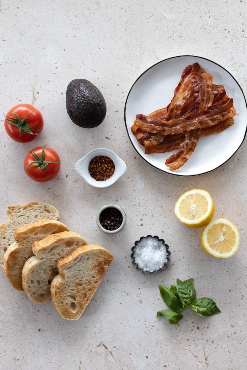 Ingredients for avocado toast with tomato in small bowls and plates on a table.