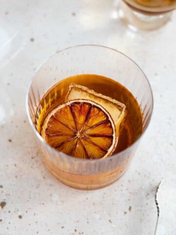Blood orange old fashioned in a cocktail glass, garnished with dried blood orange.