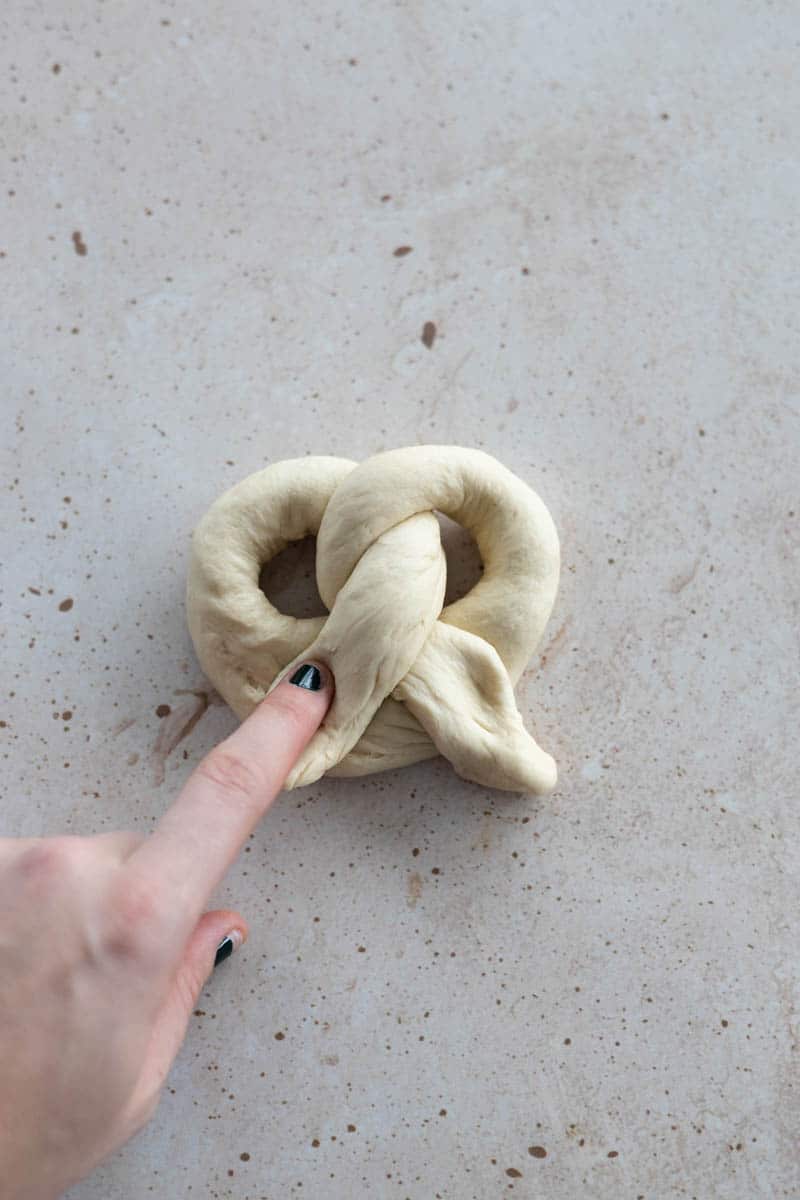 Twisting the ends of the dough rope and pushing down at the bottom of the U to make the pretzel shape.