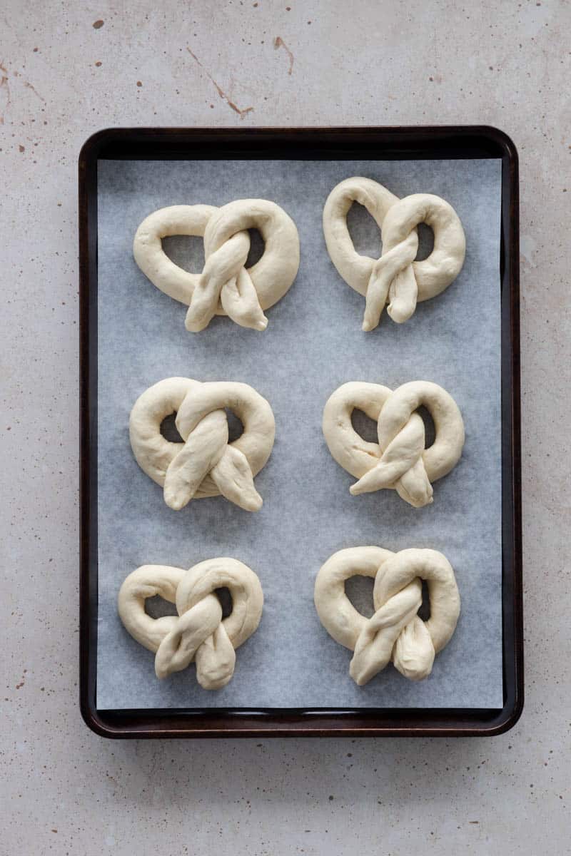 6 pretzels on a baking sheet ready to bake.