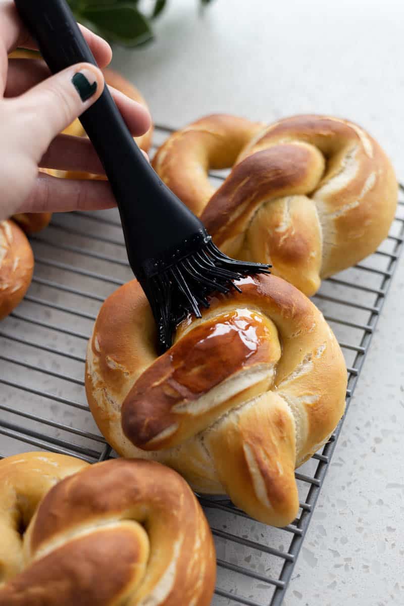 Brushing melted butter on a baked pretzel.