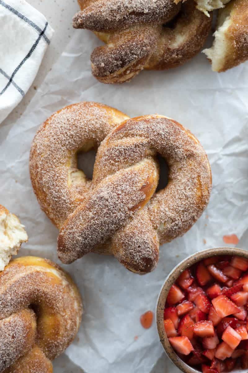 Cinnamon sugar pretzels on a piece of parchment paper with a bowl of macerated strawberries. 