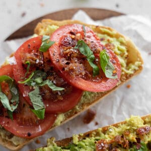 Avocado toast with tomato on a wooden cutting board.