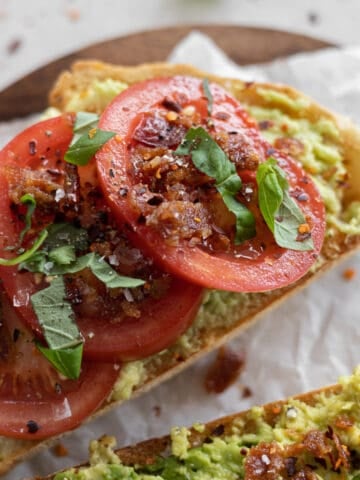 Avocado toast with tomato on a wooden cutting board.