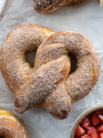 Cinnamon Sugar Pretzel on white parchment paper with a bowl of macerated strawberries.