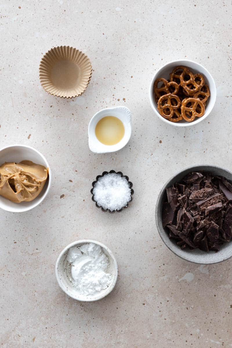 Ingredients for Dark Pretzel Peanut Butter Cups in small bowls on a table. 