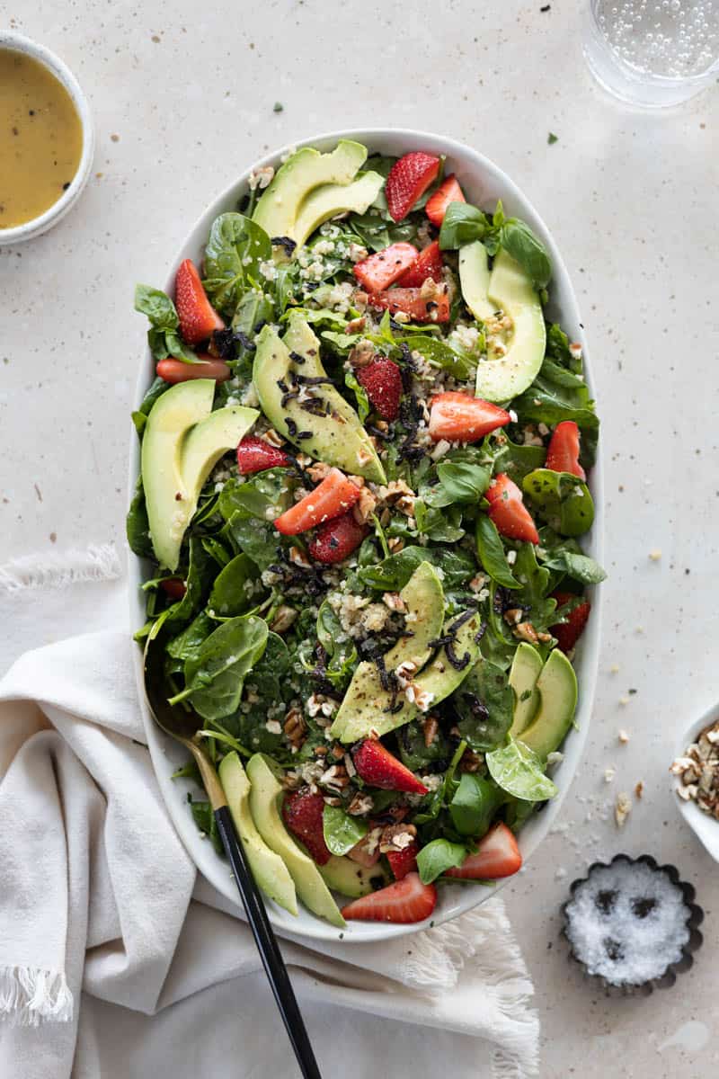 A serving plattter with Spinach and Arugula Salad with Strawberries and serving utensils on a table.