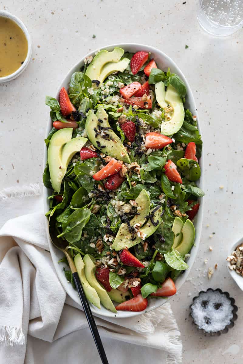 A serving plattter with Spinach and Arugula Salad with Strawberries and serving utensils on a table. 