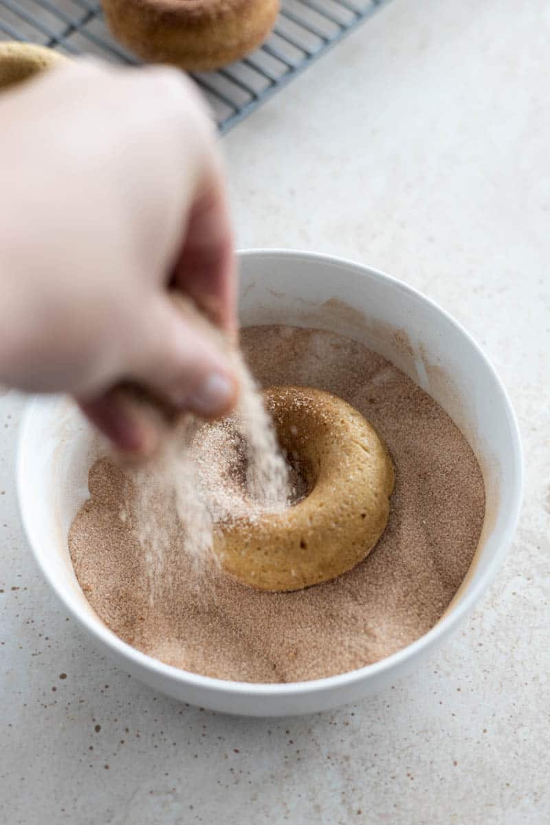 Sprinkling a donut with cinnamon sugar in a bowl.
