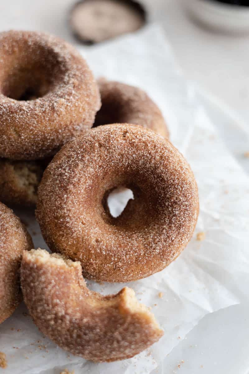 A closeup of a whole, baked Cinnamon Sugar Donut with a broken piece of donut next to it.