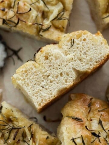 A closeup side view of a slice of focaccia with air bubbles in the dough.