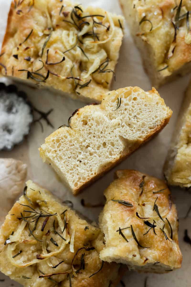 A closeup side view of a slice of focaccia with pockets of air bubbles in the bread. 