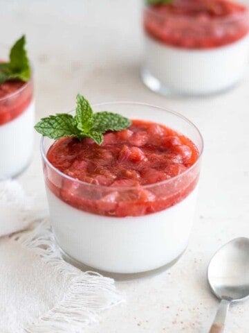 Panna cotta in small glasses topped with strawberry rhubarb compote and a mint sprig garnish.