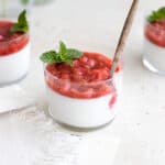 Panna cotta topped with berries in a small glass with a wooden spoon and mint sprig.