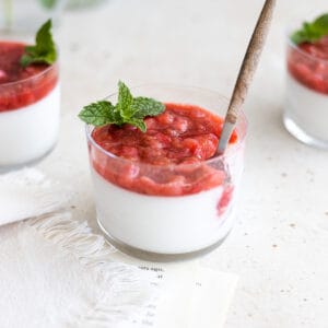 Panna cotta topped with berries in a small glass with a wooden spoon and mint sprig.