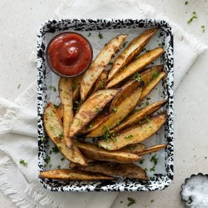 Crispy Garlic Potato Wedges on a black and white speckled tray with a small bowl of ketchup.