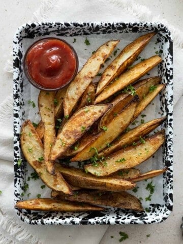 Crispy Garlic Potato Wedges on a black and white speckled tray with a small bowl of ketchup.