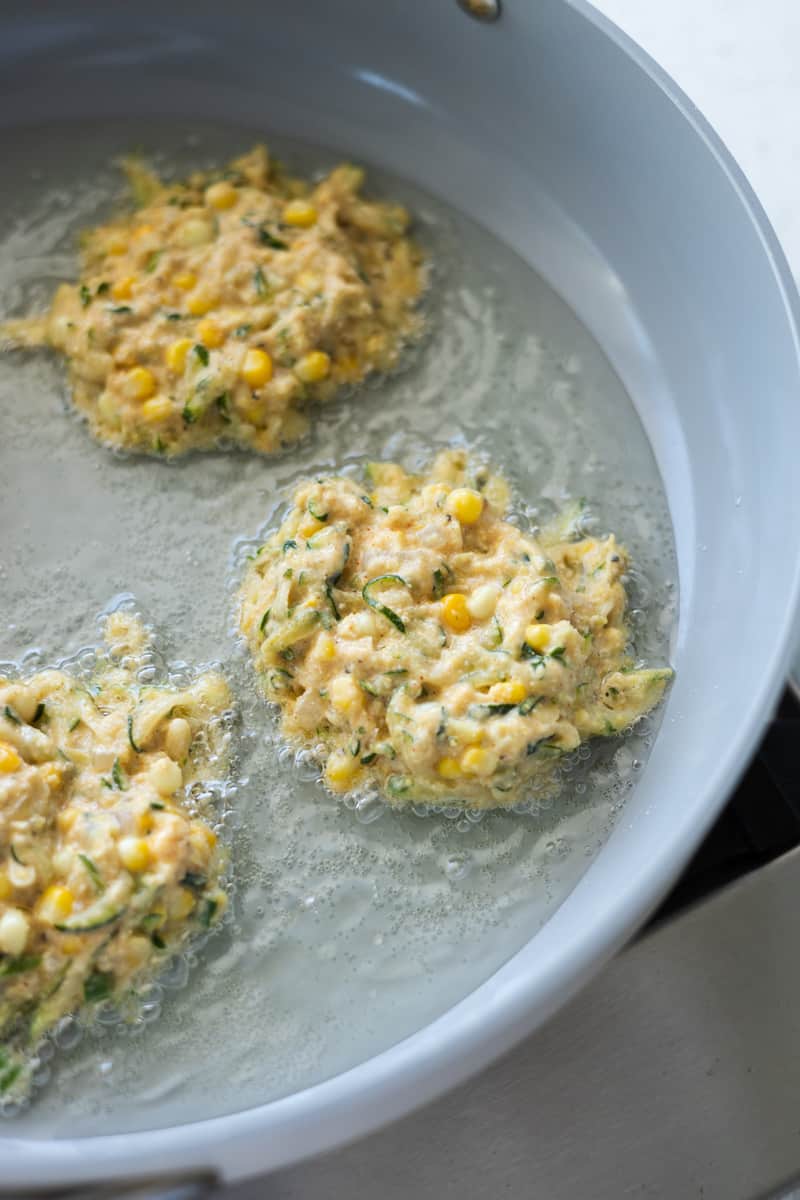 Three small fritters frying in oil in a large skillet. 